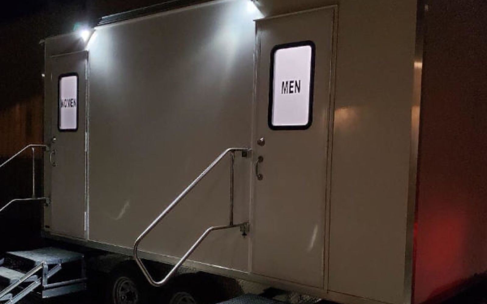 5-stall luxury bathroom trailer with lit women's and men's entries at a night event, The Lavatory NorCal