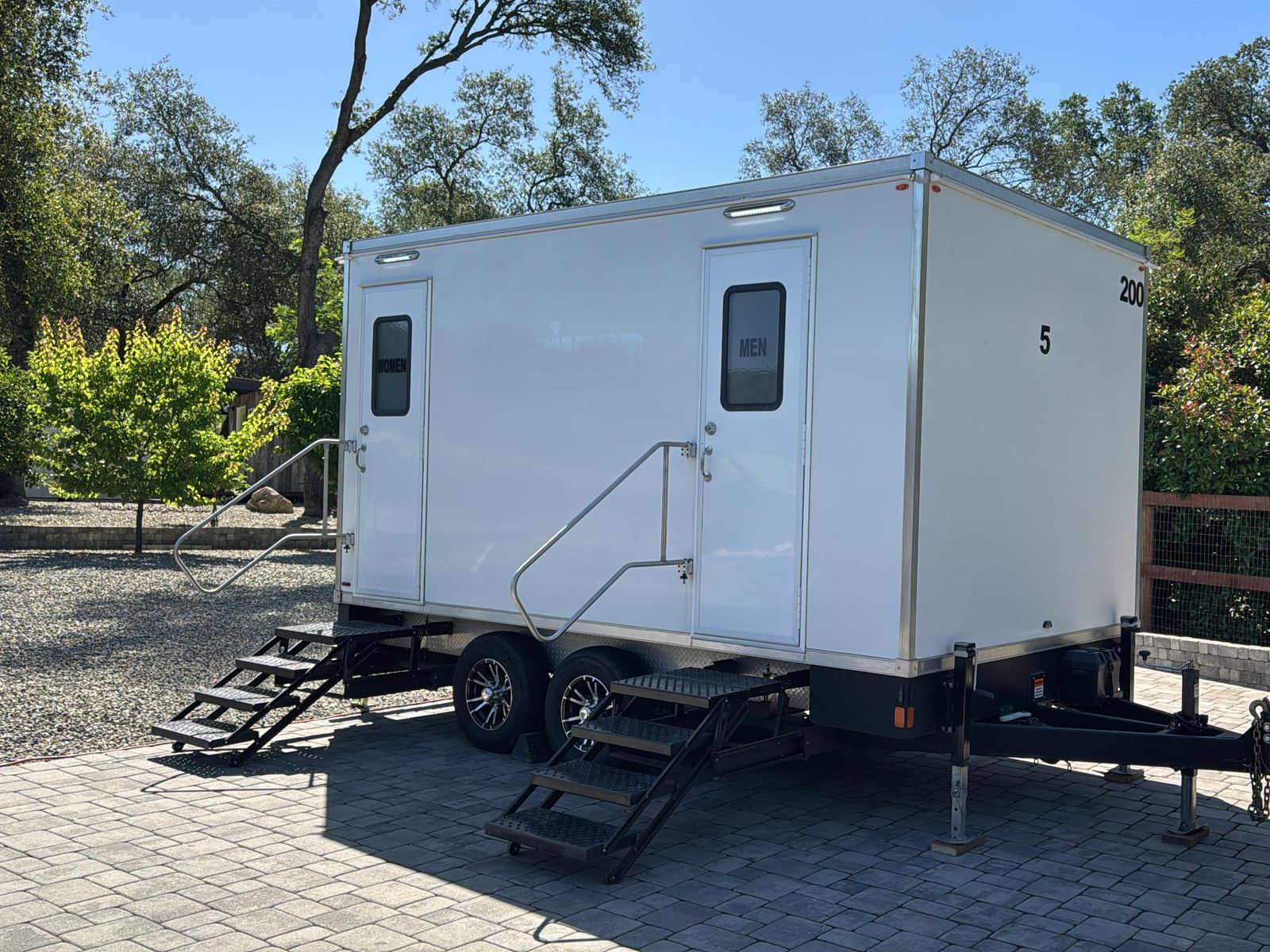 5-stall restroom trailer leveled on a paver drive under the oaks with both stairs set for a wedding in Granite Bay, The Lavatory NorCal