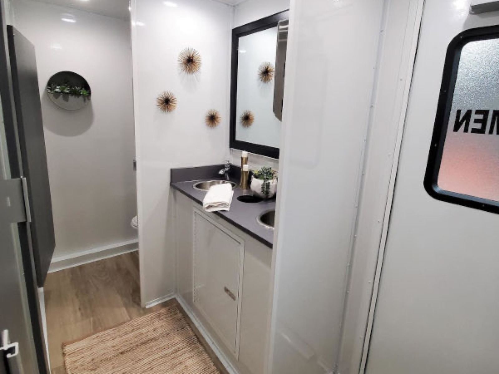 Vanity with stainless sinks, a framed mirror and wall art beside the private stalls inside a 5-stall restroom trailer, The Lavatory NorCal