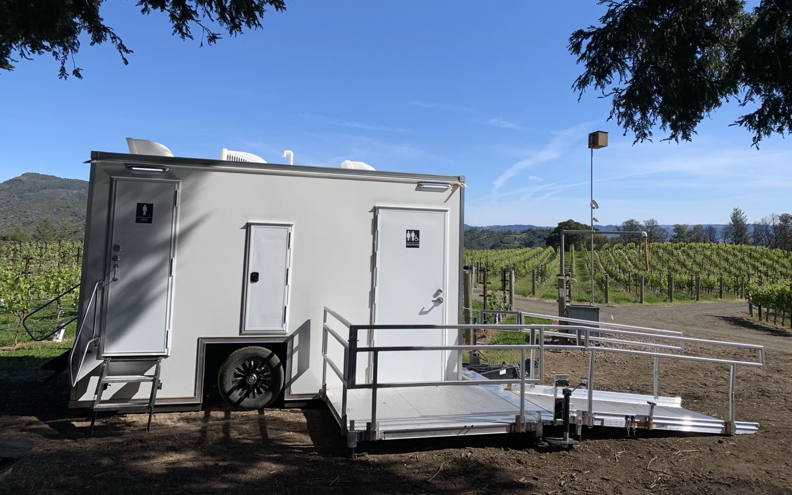 ADA plus 2 bathroom trailer with a ramp and railings at the edge of a vineyard, The Lavatory NorCal