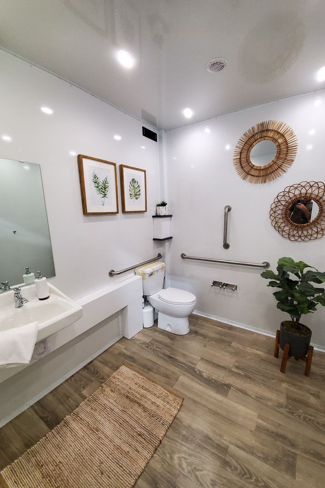 Accessible room in an ADA restroom trailer with grab bars, rattan mirrors, framed botanical prints and a wood floor, The Lavatory NorCal