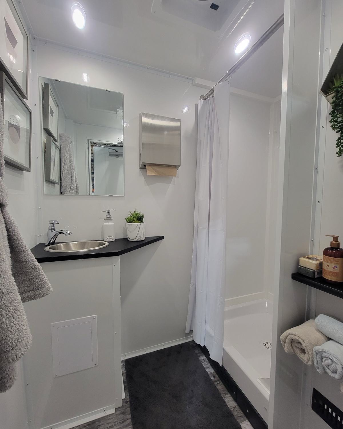 Private shower room with folded towels, a vanity sink, a mirror and framed art inside a shower trailer, The Lavatory NorCal