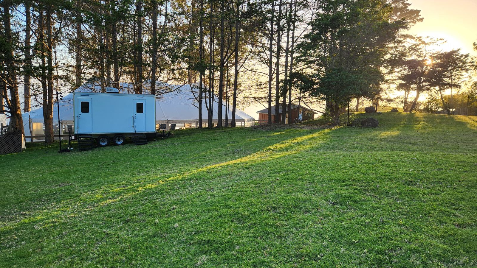 Restroom trailer beside the reception tent on a Big Sur wedding meadow at golden hour, The Lavatory NorCal