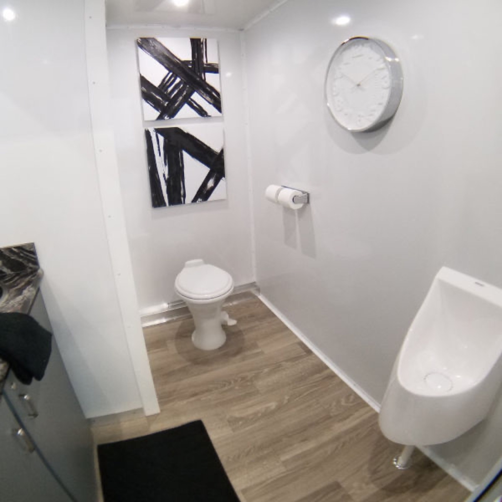 Men's room in a 2-stall bathroom trailer with a urinal, a toilet and a wall clock, The Lavatory NorCal