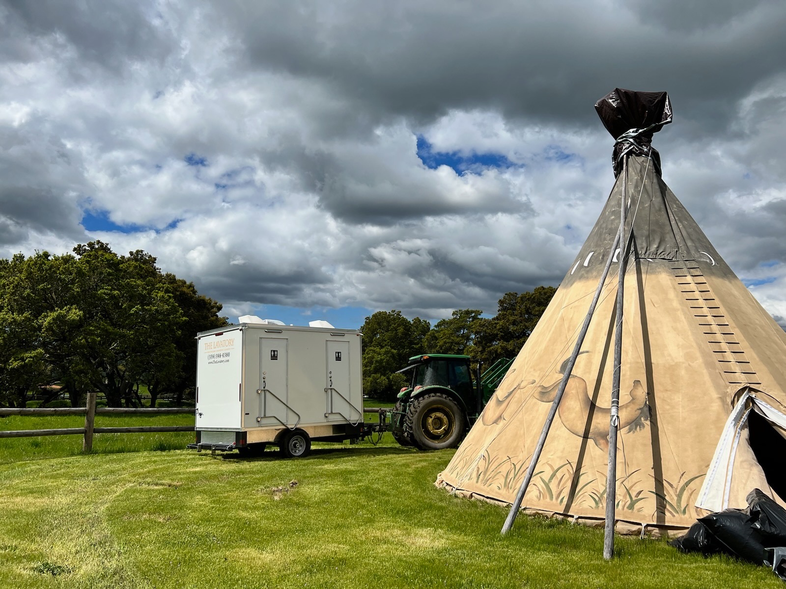 2-stall portable bathroom trailer on a ranch lawn beside a painted tipi tent, The Lavatory NorCal