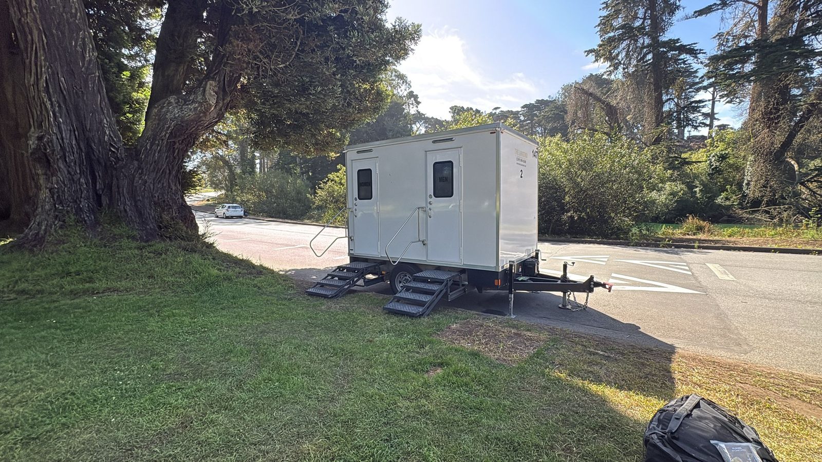2-stall bathroom trailer on the grass under cypress trees at a San Francisco park, The Lavatory NorCal