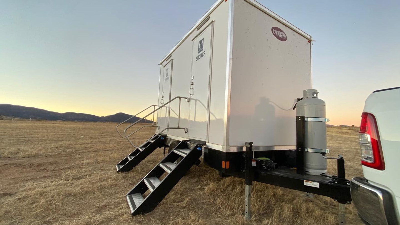 Small shower and toilet combo trailer standing in an open field at sunset, The Lavatory NorCal