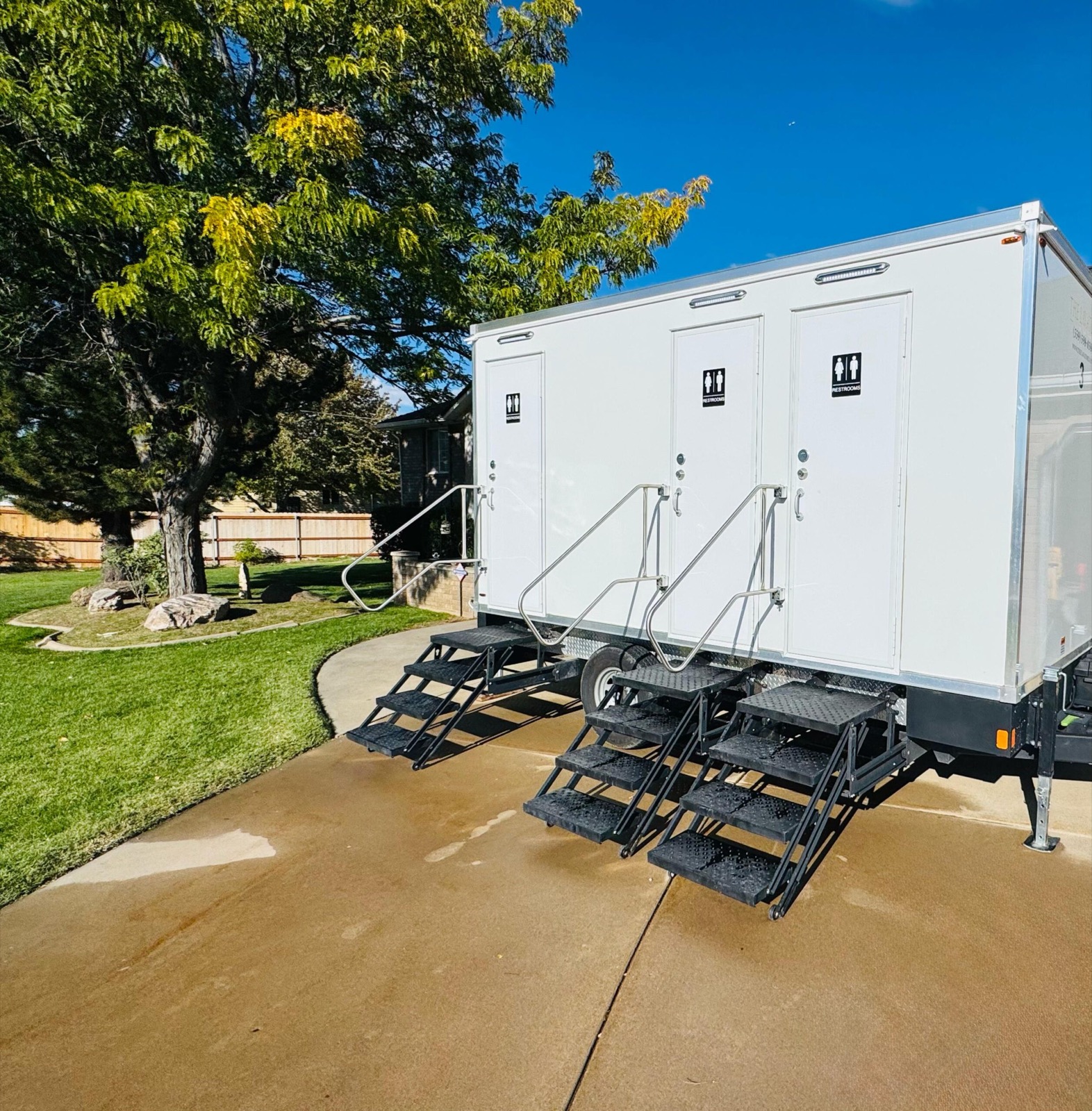 3-stall private bathroom trailer set up on a home driveway beside a green lawn, The Lavatory NorCal