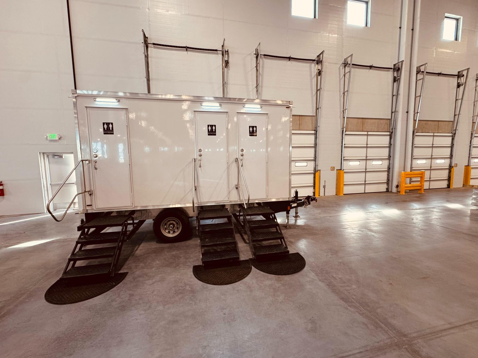 3-stall bathroom trailer with entry mats set up inside a new warehouse building, The Lavatory NorCal