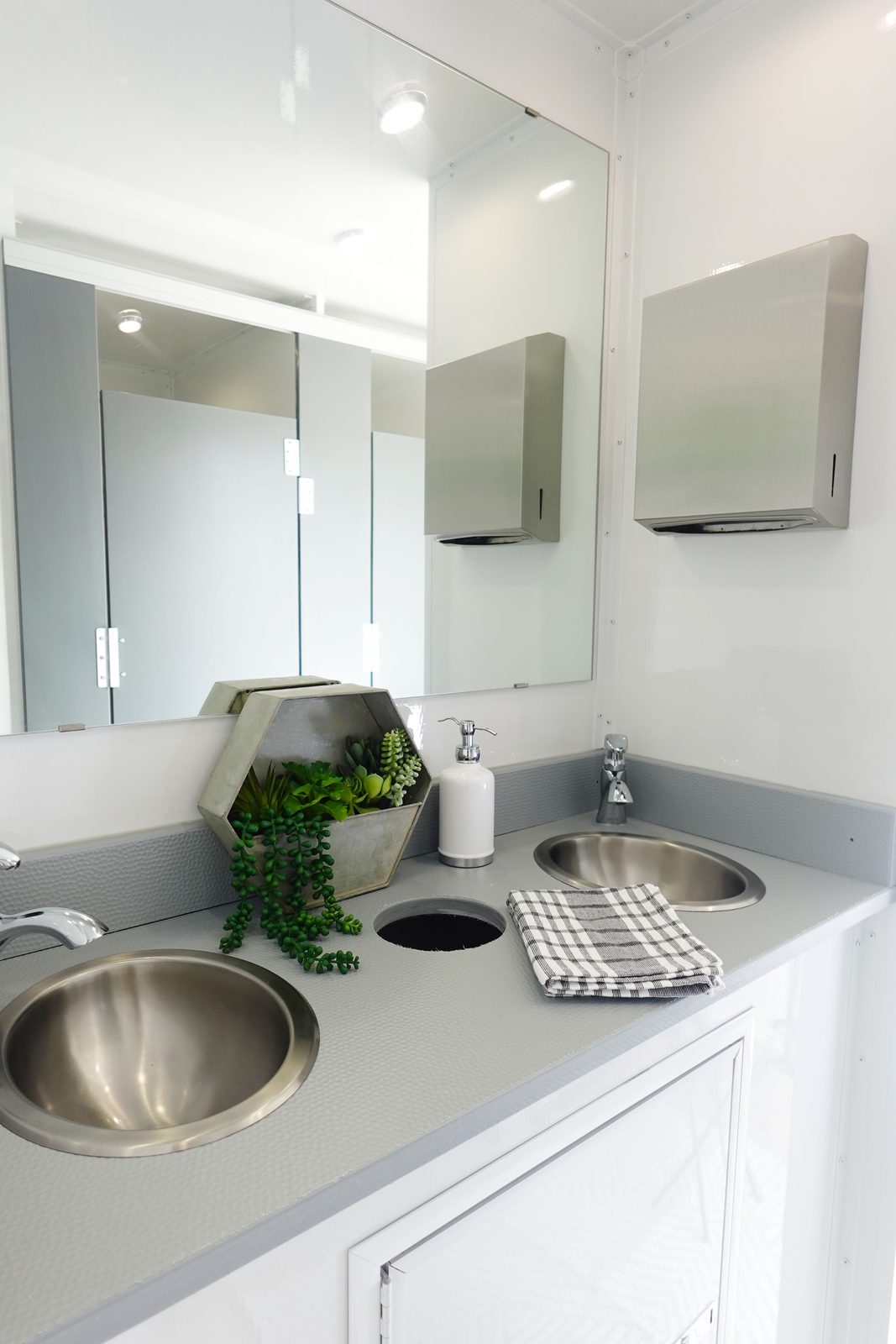 Double stainless sinks, mirror and paper towel dispensers in the women's side of a 5-stall bathroom trailer, The Lavatory NorCal