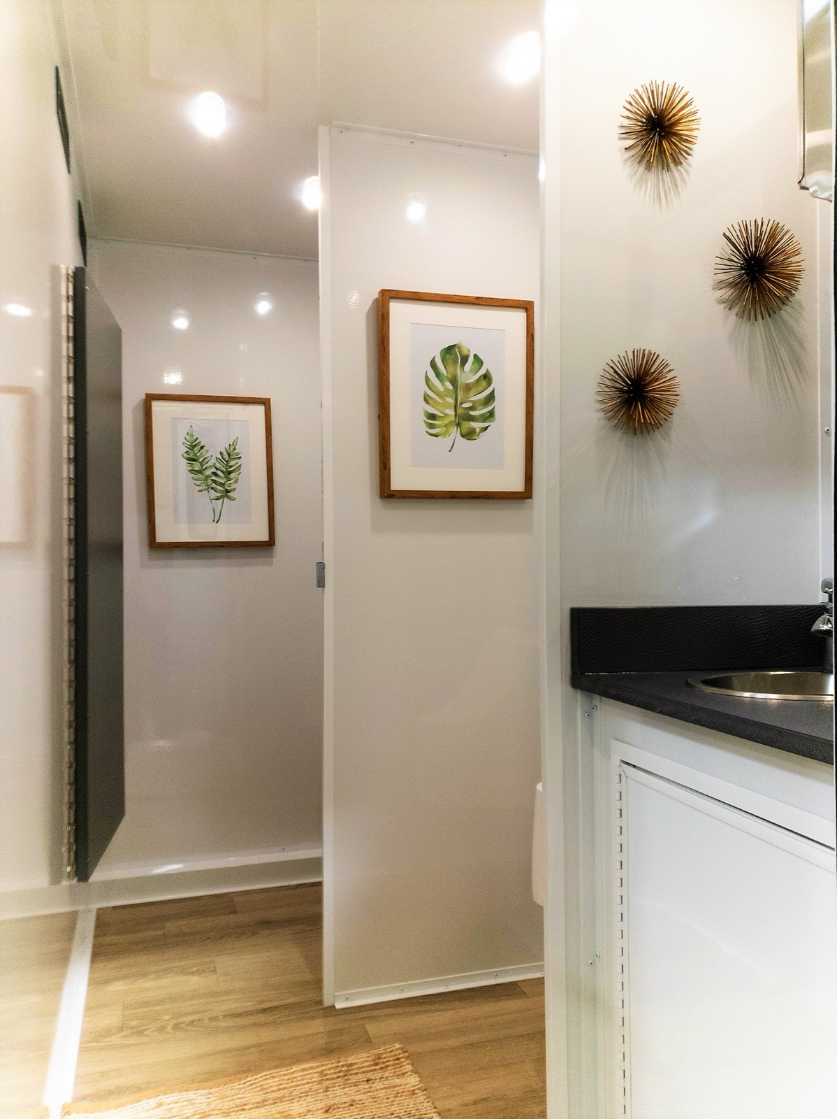 Stall hallway with botanical art and private doors inside a 5-stall portable restroom trailer, The Lavatory NorCal