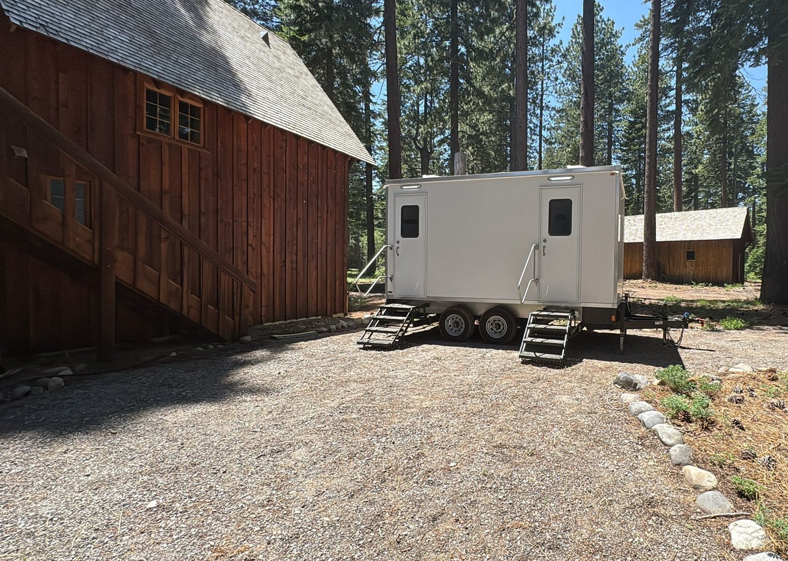 5-stall bathroom trailer on a gravel pad among tall pines beside a wooden barn near Lake Tahoe, The Lavatory NorCal