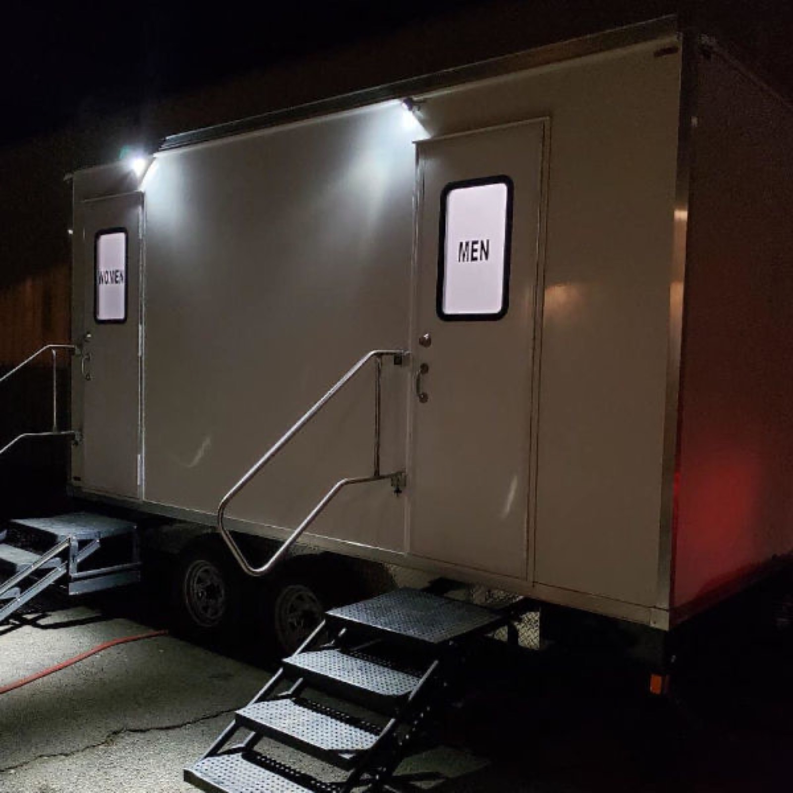 5-stall deluxe restroom trailer with lit women's and men's doors set up for an evening event, The Lavatory NorCal