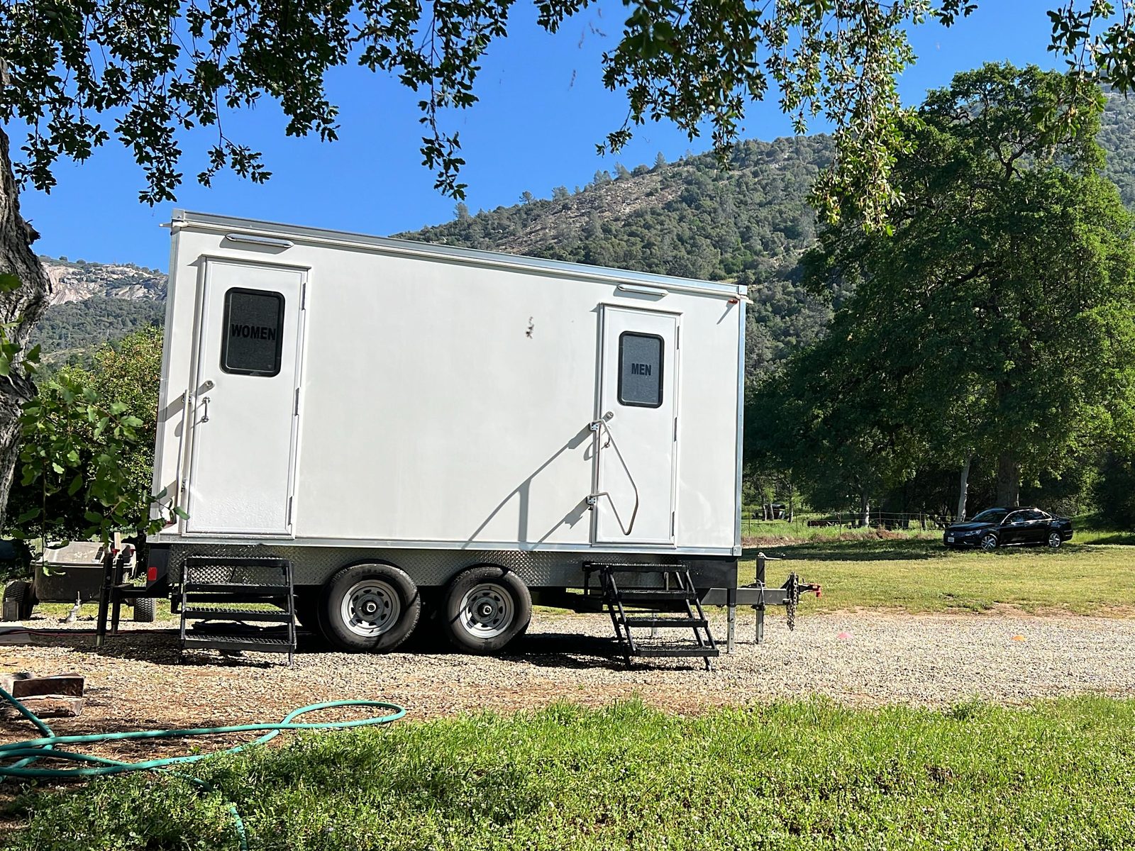 5-stall bathroom trailer with women's and men's doors on a gravel pad under oak trees in the foothills, The Lavatory NorCal