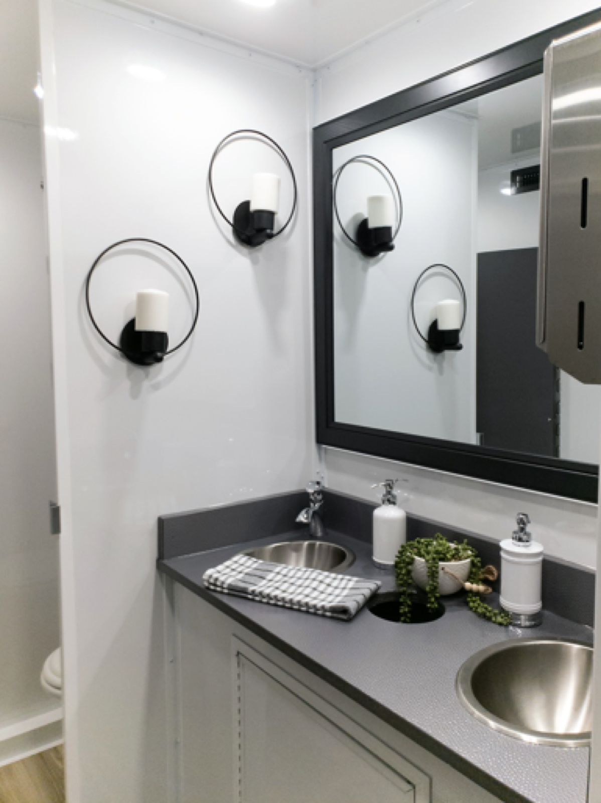 Double sink vanity with a framed mirror and wall sconces inside a 5-stall luxury restroom trailer, The Lavatory NorCal