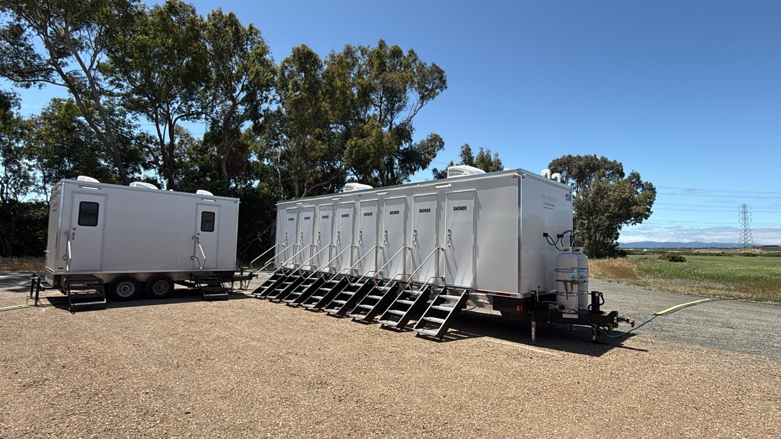 8-stall shower trailer beside a bathroom trailer on a gravel job site under eucalyptus trees, The Lavatory NorCal