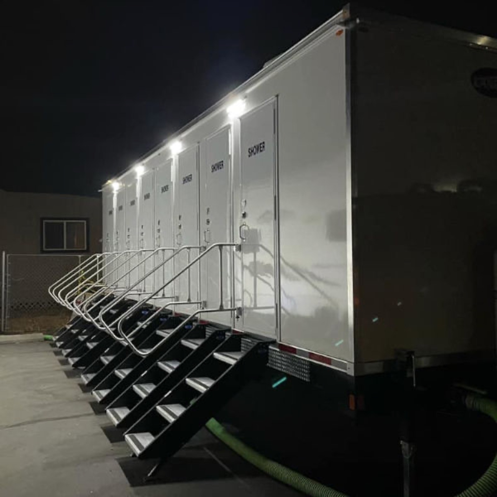 Shower trailer lit at night with lights over every shower door at a work site, The Lavatory NorCal