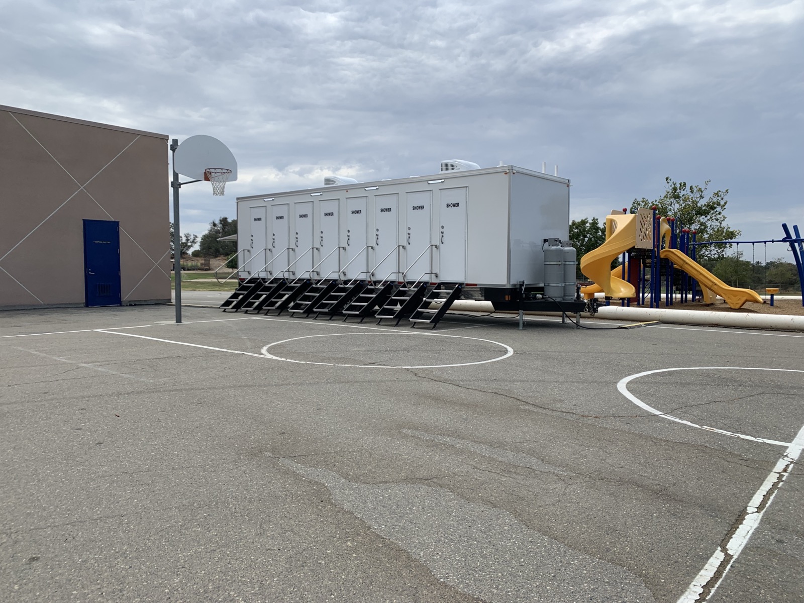 8-stall shower trailer parked on a school blacktop beside a playground during a relief effort, The Lavatory NorCal