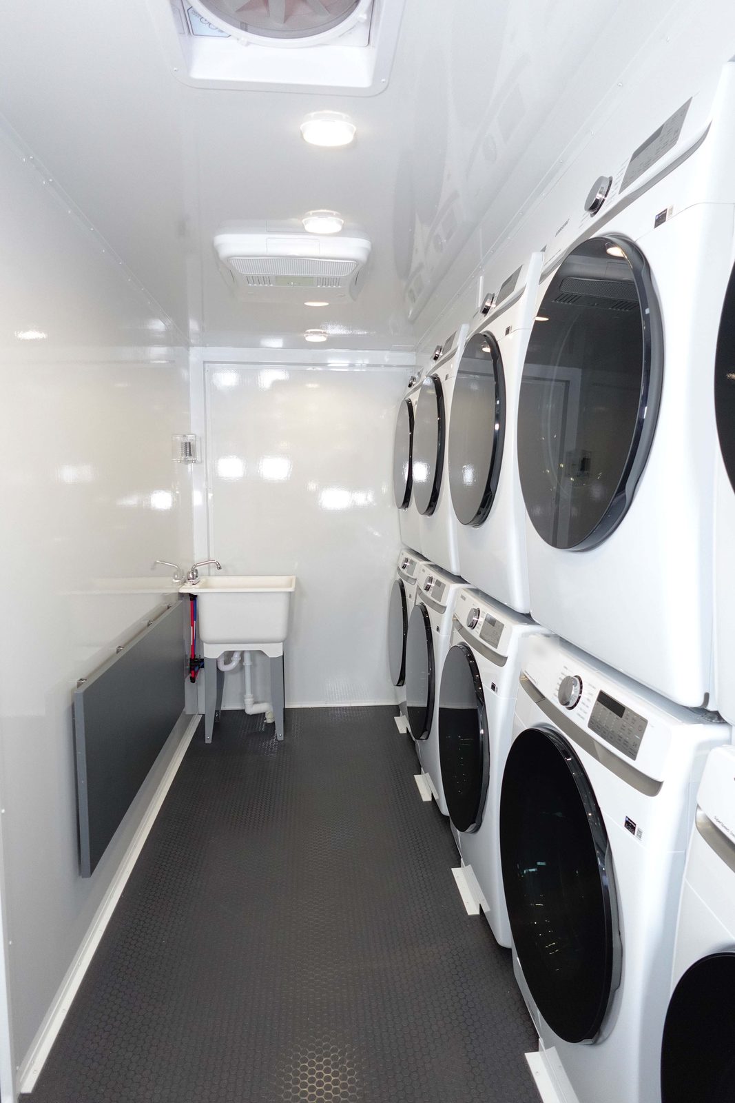 Stacked washers and dryers down one side of the 8-station laundry trailer, with a utility sink and fold-down table, The Lavatory NorCal