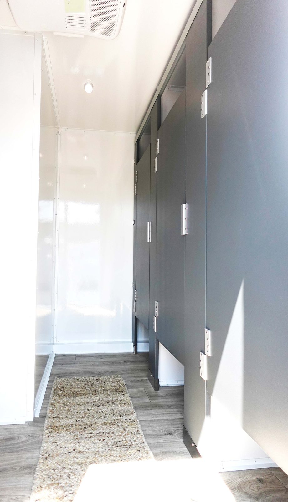 Row of private stall partitions with a runner rug inside a 9-stall bathroom trailer, The Lavatory NorCal