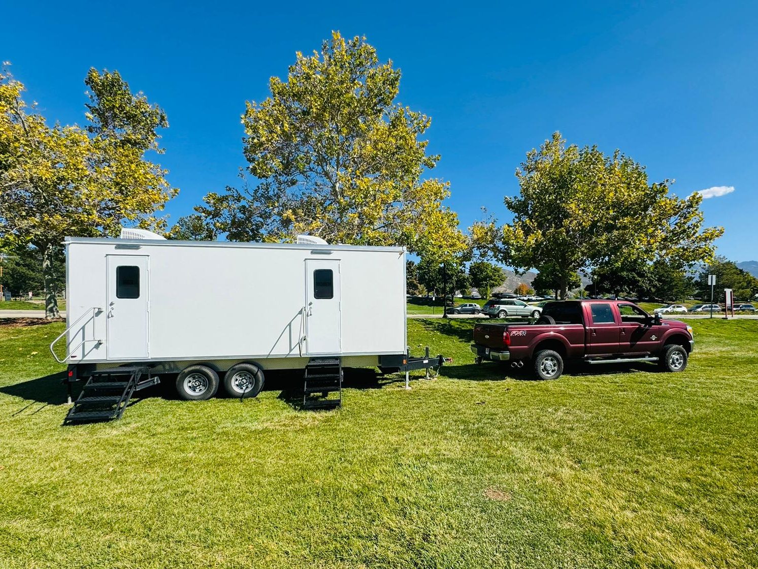 9-stall bathroom trailer with two entry doors, steps and two roof AC units on a park lawn, The Lavatory NorCal