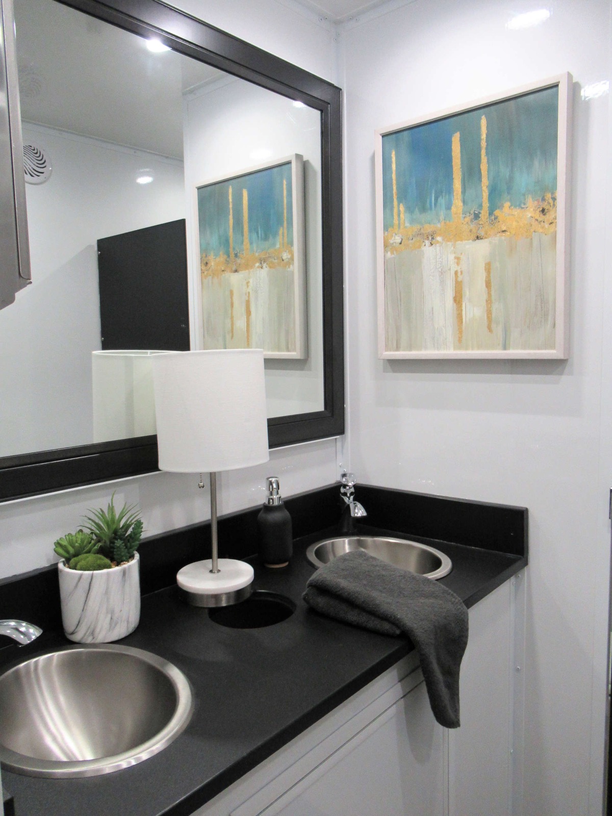 Double sink vanity with a lamp and abstract art inside a 9-stall deluxe bathroom trailer, The Lavatory NorCal
