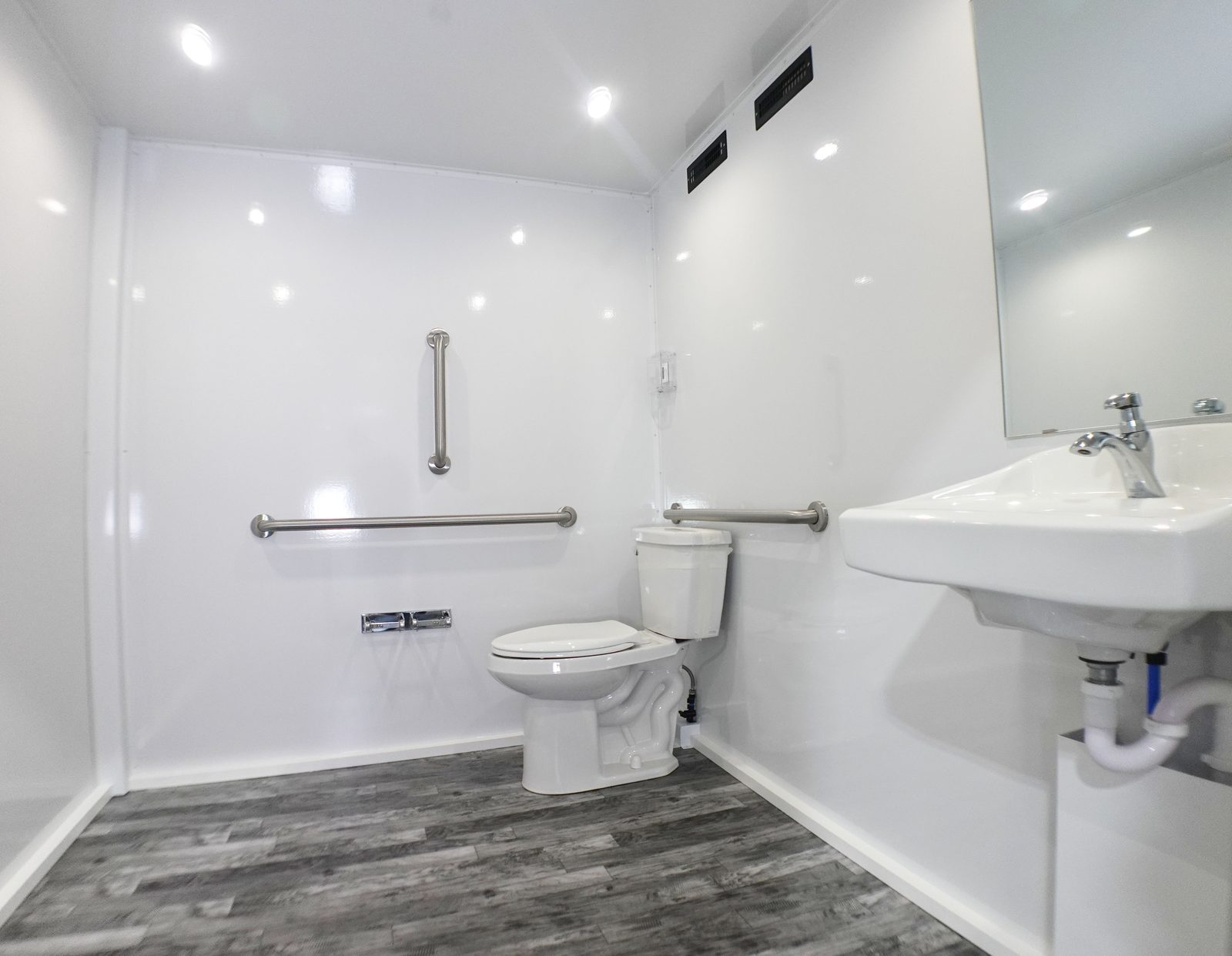 Accessible room in the ADA plus 2 bathroom trailer with grab bars around the toilet and a wall-mounted sink, The Lavatory NorCal