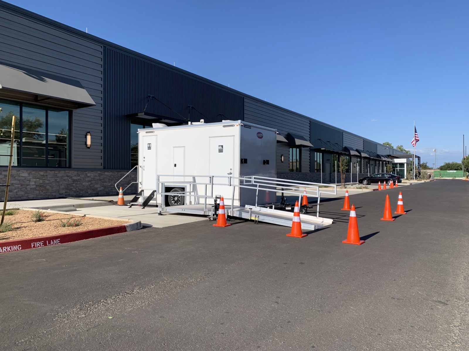 Accessible bathroom trailer with a ramp and safety cones outside an office park, The Lavatory NorCal