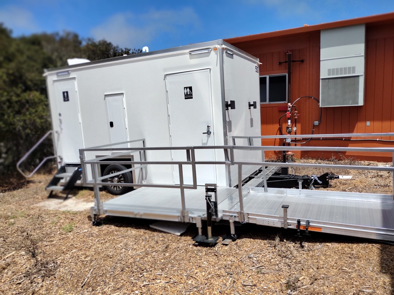 ADA plus 2 bathroom trailer with a ramp beside a school classroom building for staff and students, The Lavatory NorCal