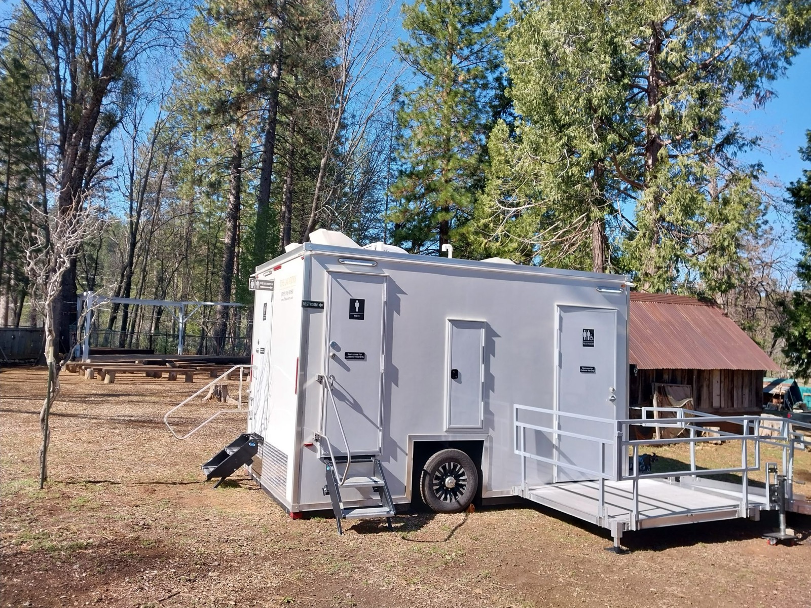 ADA plus 2 bathroom trailer with a ramp parked at a pine forest camp, The Lavatory NorCal