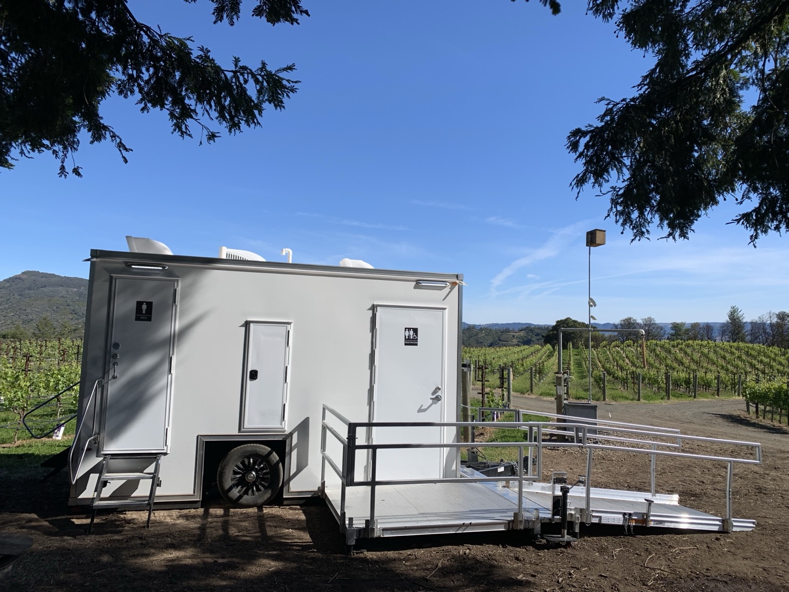ADA plus 2 bathroom trailer with an aluminum ramp set at the edge of a vineyard, The Lavatory NorCal