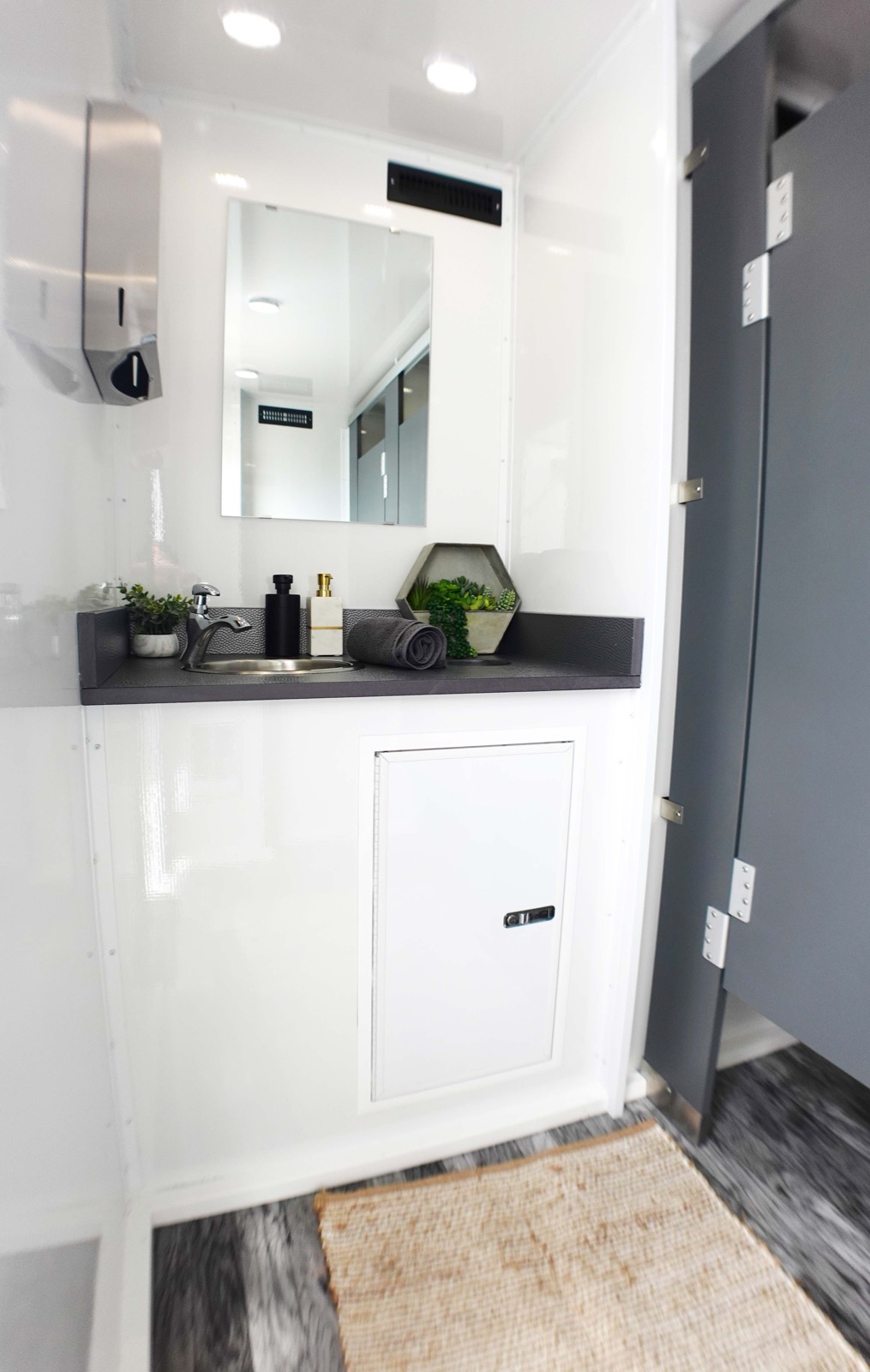 Vanity and mirror beside a stall door inside an ADA plus 6 restroom trailer, The Lavatory NorCal