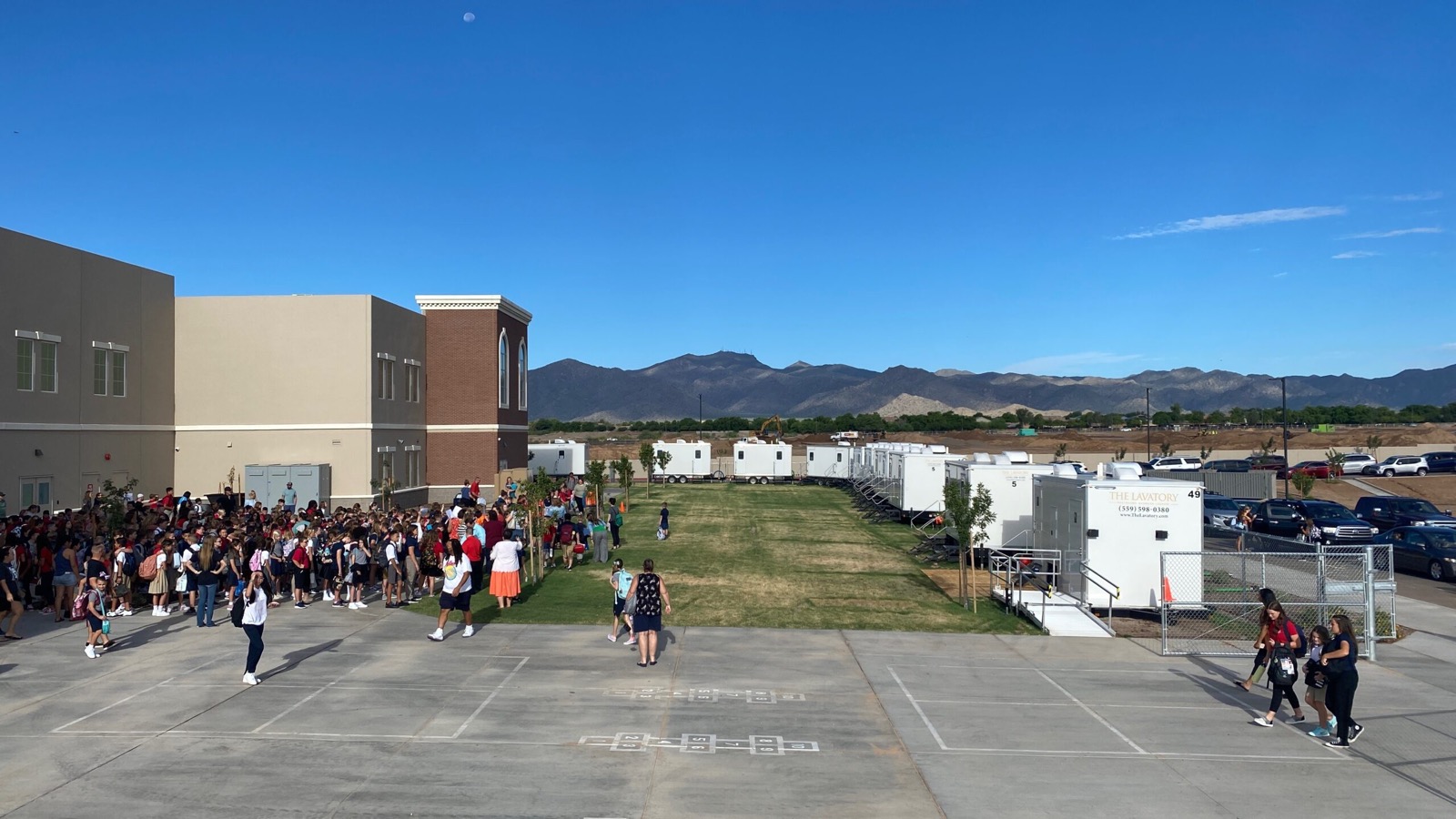 Students and staff gathering outside a school next to a row of restroom trailers, The Lavatory NorCal