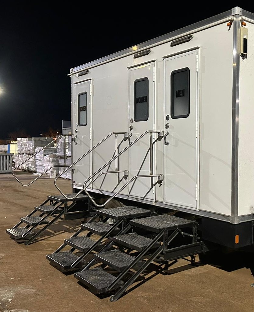 3-stall portable bathroom trailer with three sets of railed steps set up at night on a North Valley jobsite yard, The Lavatory NorCal