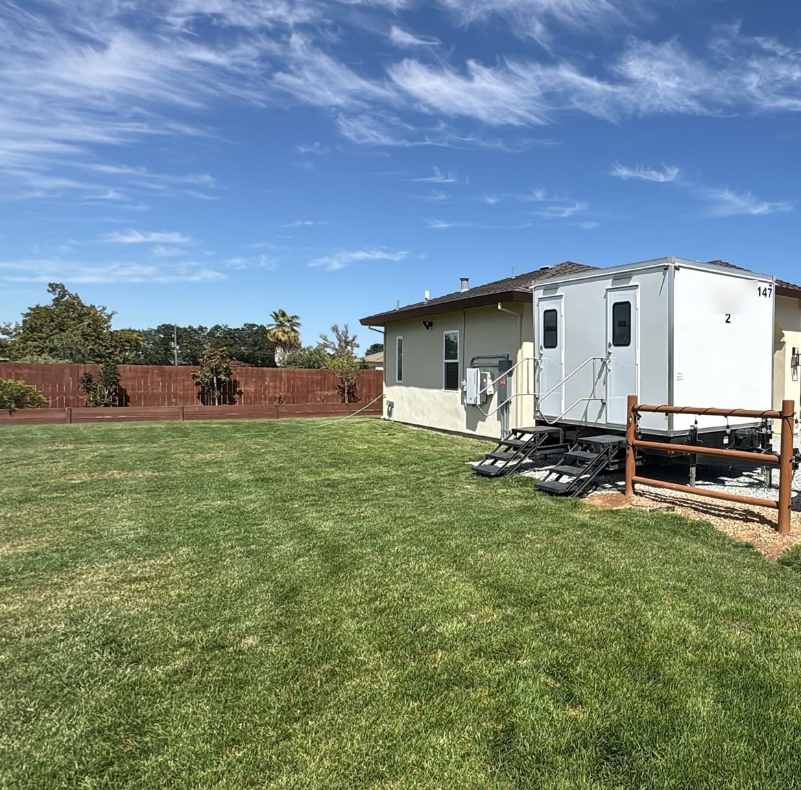 2-stall bathroom trailer set beside a house next to a big green lawn for a family party near Galt, south of Elk Grove, The Lavatory NorCal