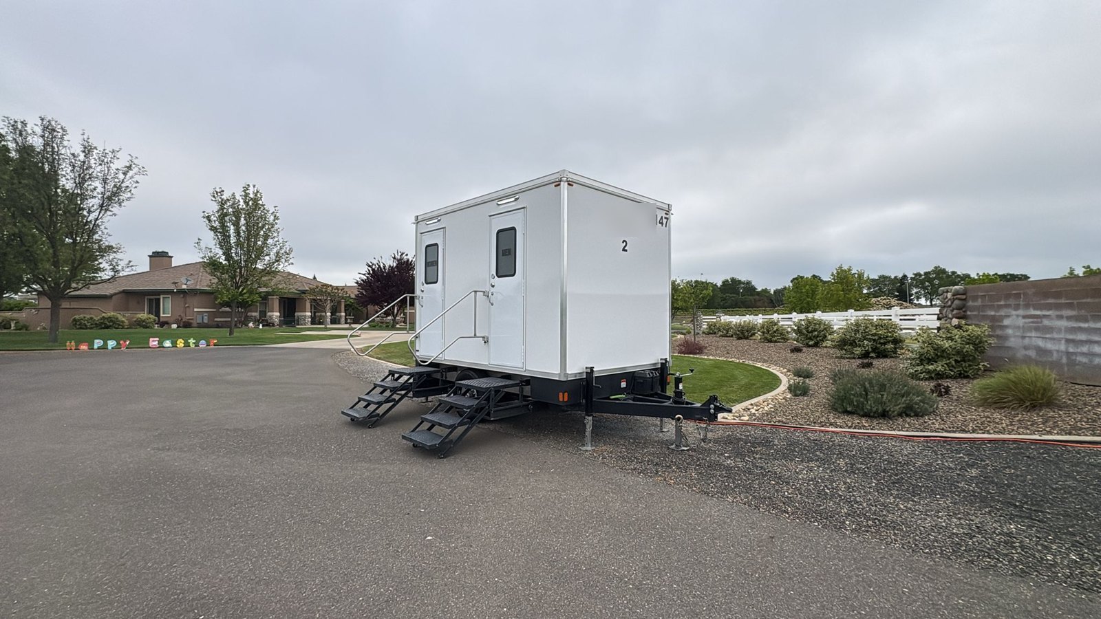 2-stall portable bathroom trailer on a paved ranch drive beside landscaping and a white fence near Wilton, east of Elk Grove, The Lavatory NorCal
