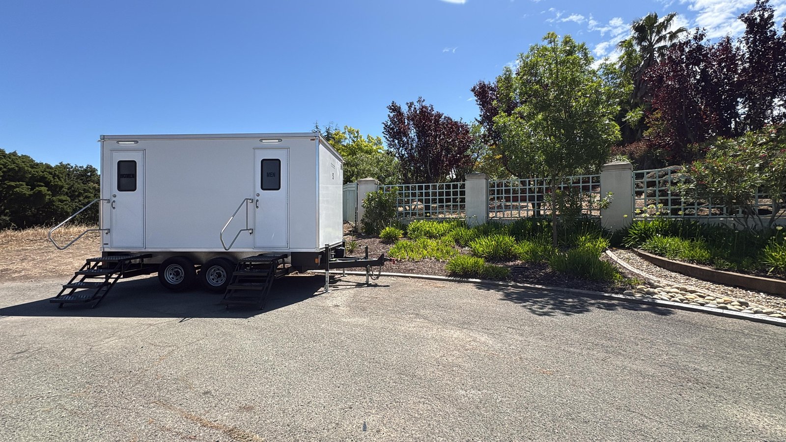 Climate-controlled restroom trailer with women's and men's doors and steel stairs on the drive of a Fremont hillside estate, The Lavatory NorCal