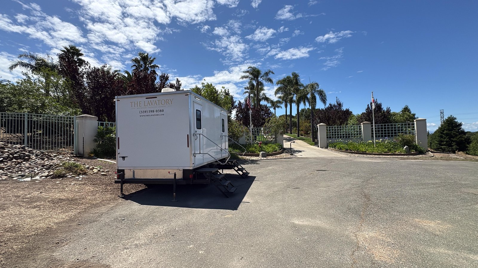 Portable restroom trailer parked by the gated entry of a hillside estate in Fremont under tall palm trees, The Lavatory NorCal