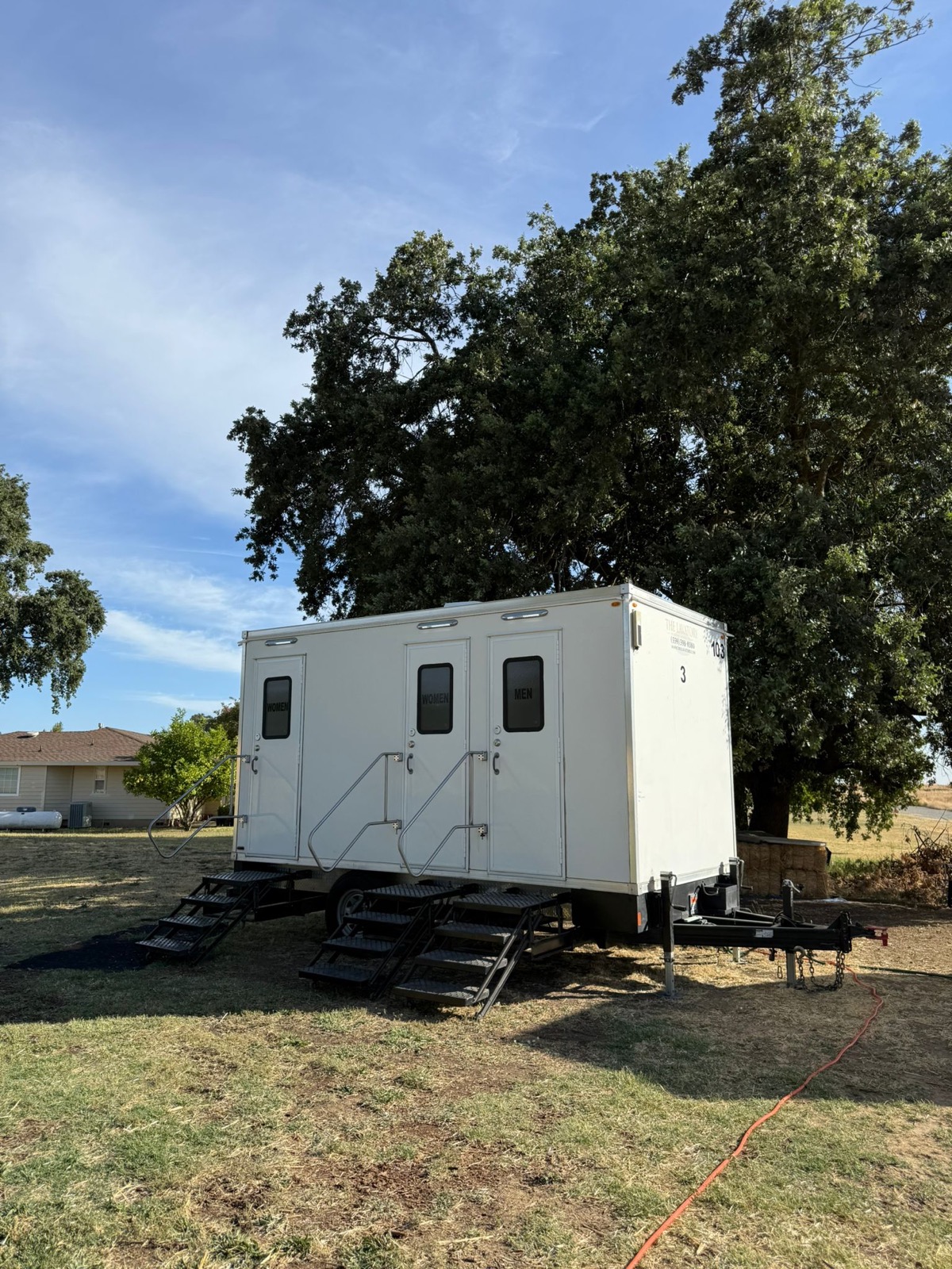 3-stall portable bathroom trailer leveled on a lawn under a valley oak for a Sacramento wedding, The Lavatory NorCal