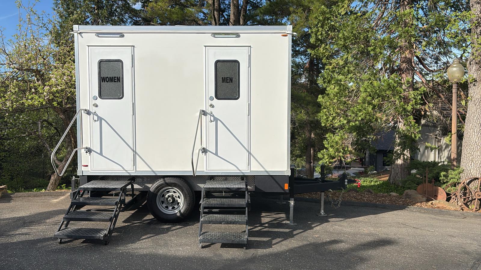 2-stall portable bathroom trailer parked under pines at a Gold Country venue in Auburn, The Lavatory NorCal