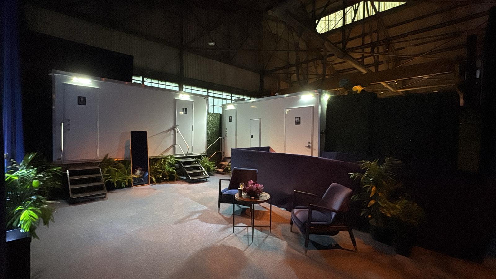 Two luxury restroom trailers lit up inside a San Francisco warehouse event space with a lounge, plants and a full-length mirror, The Lavatory NorCal