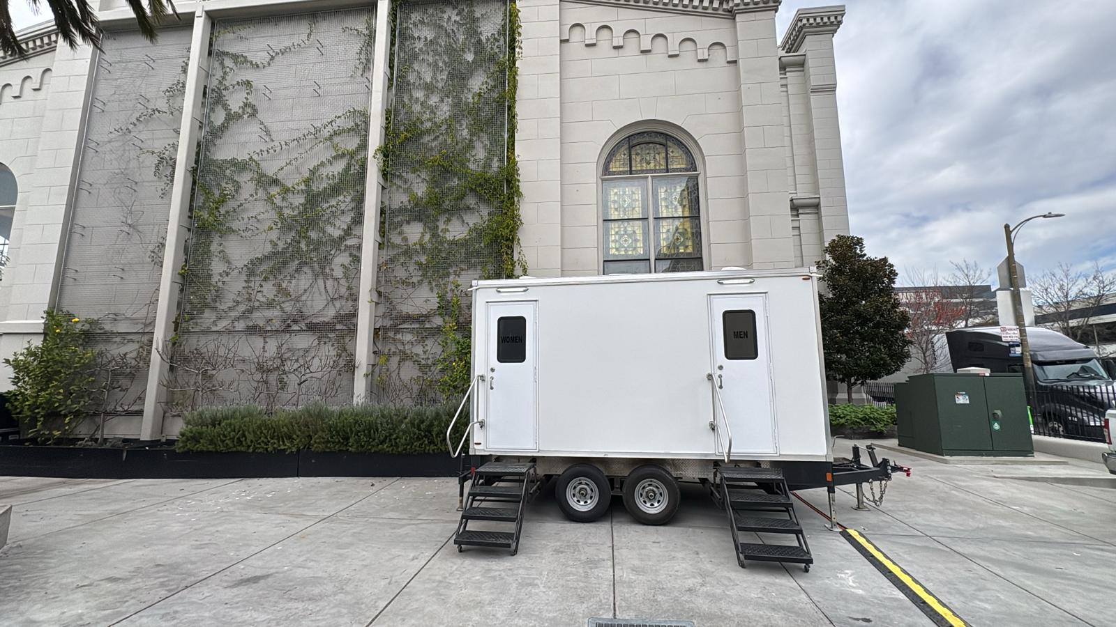 5-stall restroom trailer with women's and men's doors parked on a concrete plaza beside a historic church in San Francisco, The Lavatory NorCal