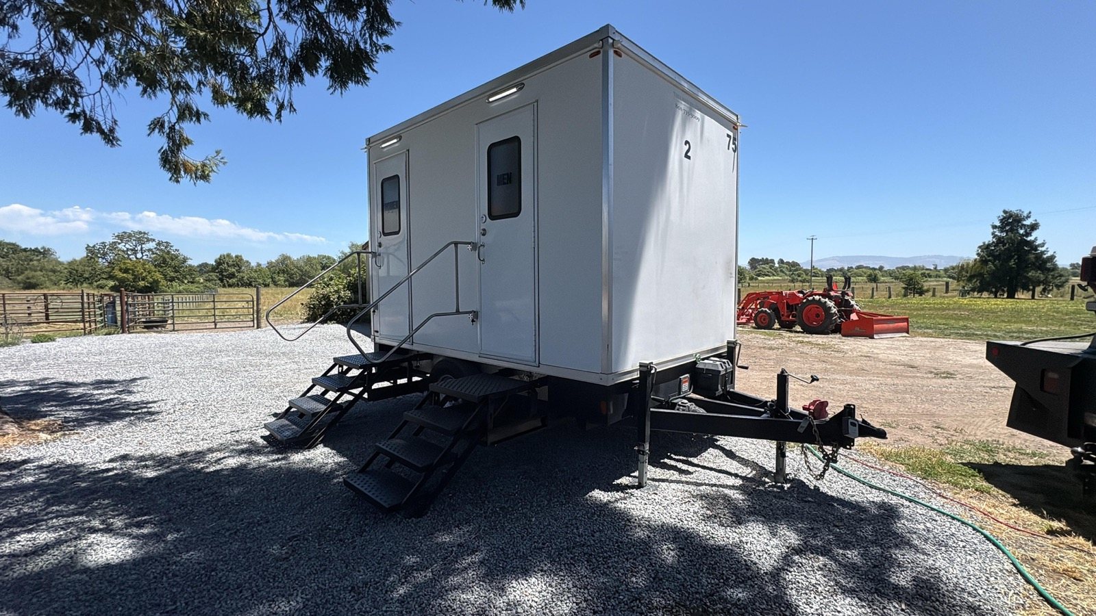 2-stall portable bathroom trailer with men's and women's doors set on gravel at a Santa Rosa ranch, The Lavatory NorCal
