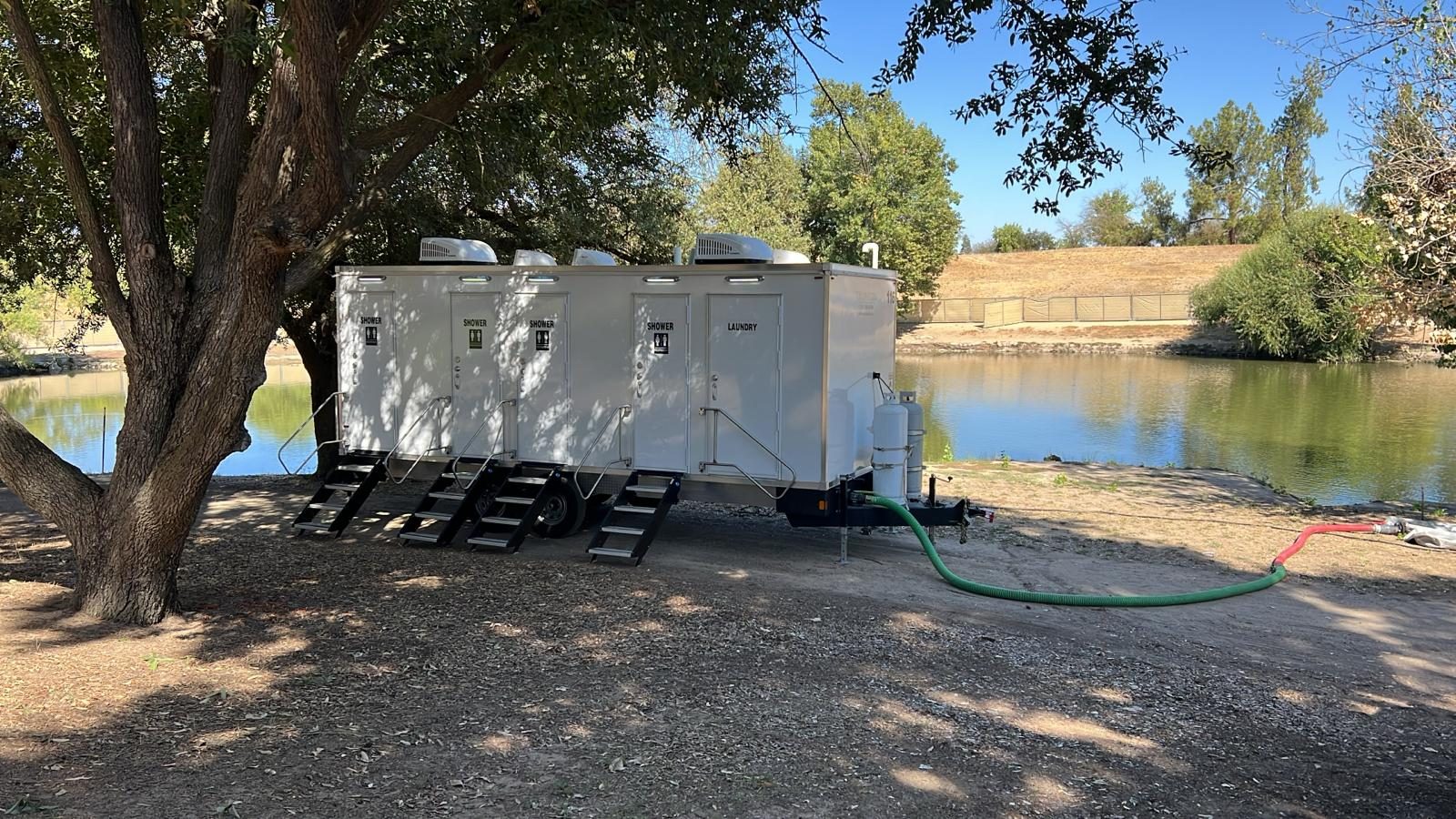 4-station shower, restroom and laundry combo trailer in the shade of an oak beside a pond, The Lavatory NorCal