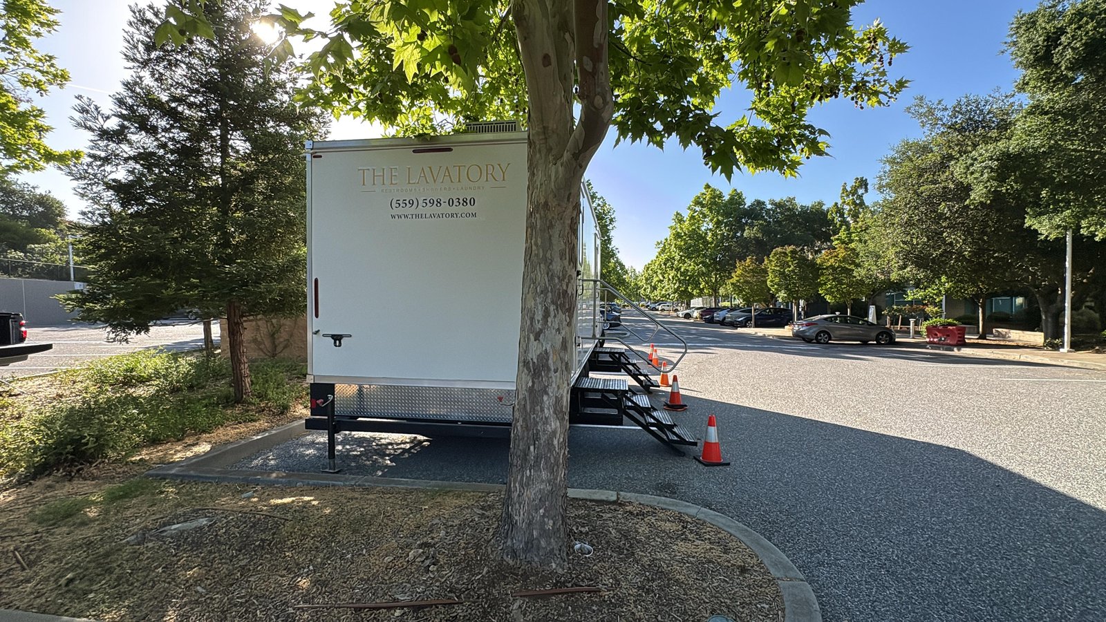 Bathroom trailer set under a sycamore with safety cones at a Silicon Valley office park, The Lavatory NorCal