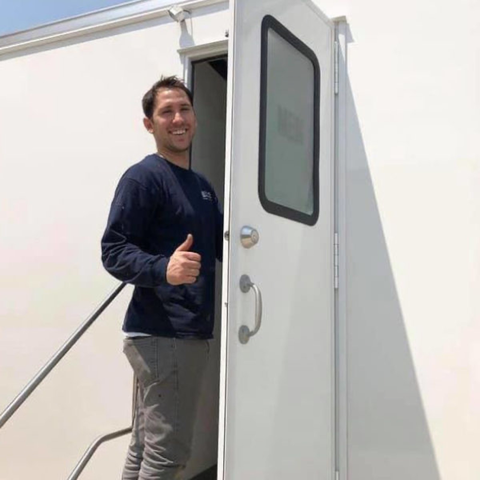 Our team member smiling with a thumbs up in the doorway of a clean bathroom trailer, The Lavatory NorCal