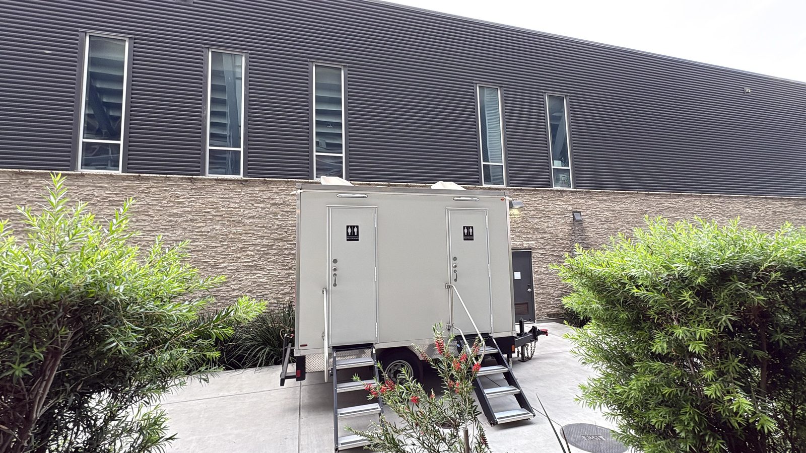 Two-door restroom trailer set in a landscaped courtyard beside an office building in San Jose, The Lavatory NorCal