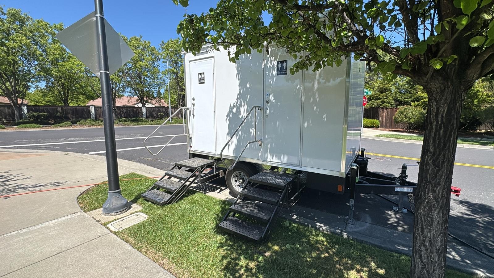 2-stall restroom trailer parked on a grass strip under a shade tree on a quiet Fairfield street, The Lavatory NorCal