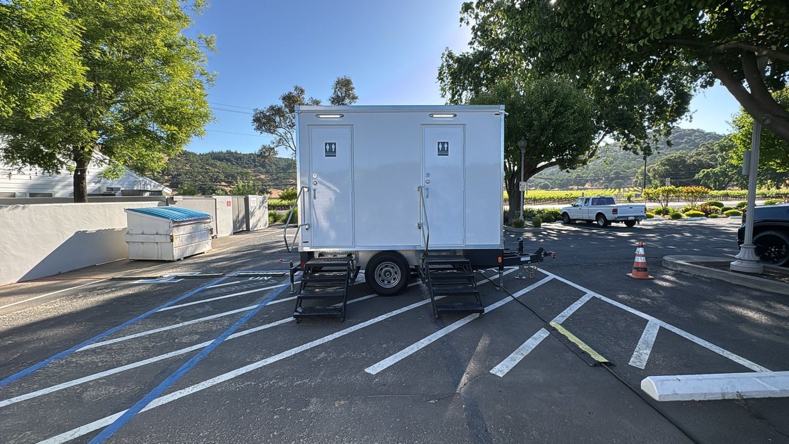 2-stall portable bathroom trailer with two restroom doors on a winery lot with vineyard hills behind, north of Vallejo, The Lavatory NorCal